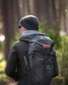 a man with a back pack walking through the woods wearing sunglasses and a beanie