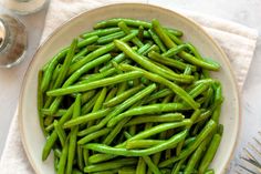 a white plate topped with green beans next to a fork and glass of water on top of a table