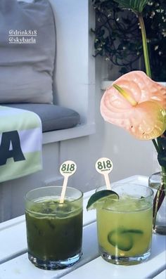 two glasses filled with green drinks sitting on top of a table next to each other