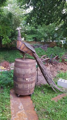 an old barrel with a peacock on top in a yard next to trees and bushes