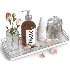 an assortment of personal care items on a clear tray with flowers and glass containers next to it