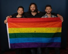 two men holding a rainbow flag with writing on it