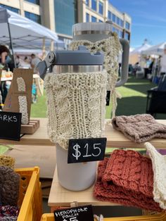 a coffee cup with a knitted cover and price tags on it at an outdoor market