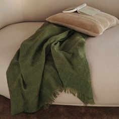 a green blanket sitting on top of a couch next to a pillow and a book