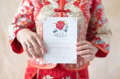 a woman in a red and gold chinese dress holding up a card with an image of a bird on it