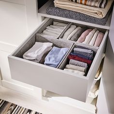 an open drawer with folded towels and folded clothes in the bottom section, on top of a striped rug