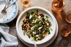 a white plate topped with a salad next to two glasses and silverware on top of a wooden table