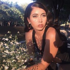 a woman sitting on a bench with flowers in front of her and looking at the camera