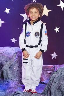 a young boy in an astronaut suit standing on stage with stars around him and smiling at the camera