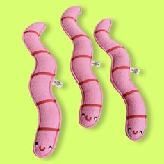 three pink worms with red strips on them, one is smiling and the other has eyes