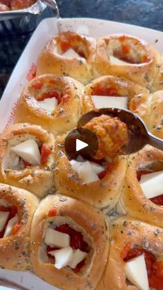 a tray filled with pizza rolls covered in cheese and tomato sauce next to a serving spoon