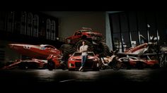 a man standing in front of a large monster truck next to two red sports cars