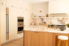 a kitchen with white cabinets and marble counter tops, an oven and stools in front of it