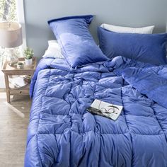 a blue comforter on a bed next to a night stand with a book and lamp