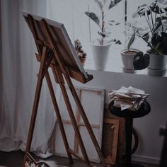 an easel sitting in front of a window next to a potted plant