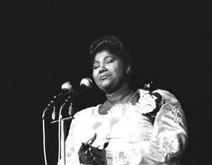 a black and white photo of a woman standing at a podium in front of microphones