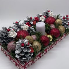 a christmas centerpiece with pine cones, ornaments and candlesticks in a red box