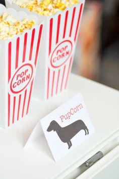 two popcorn bags with dogs on them sitting on top of a white table next to a box of popcorn