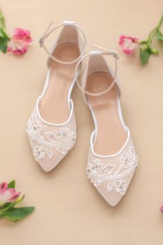 wedding shoes with white lace and flowers on the floor in front of pink flower petals