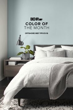 there is a bed with white sheets and pillows on top of it, in front of a blue wall that says behrt color of the month