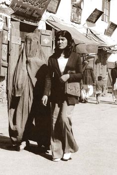 an old photo of two women walking down the street in front of a storefront