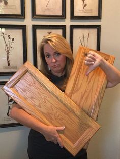 a woman is holding two large pieces of wood in front of her face and several framed pictures on the wall behind her