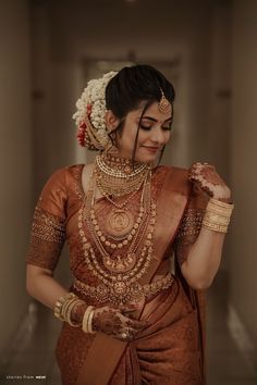 a woman in an orange and gold sari with jewelry on her neck, holding something up to her ear