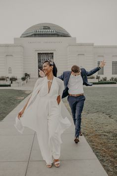 a man and woman walking down a sidewalk in front of a white building with a domed roof