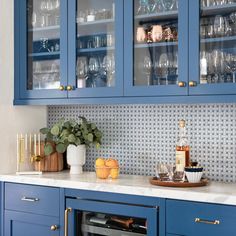 a kitchen with blue cabinets and white counter tops, filled with wine glasses and bottles