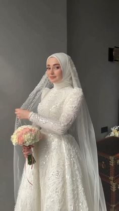 a woman in a white wedding dress and veil standing next to a table with flowers