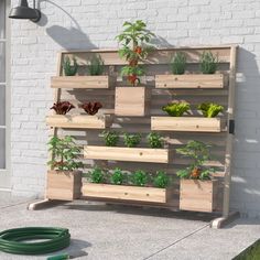 a wooden planter filled with lots of plants next to a white brick wall and green hose