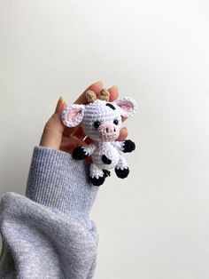 a hand holding a tiny crocheted cow on it's finger