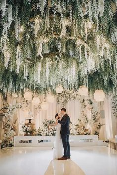 a bride and groom standing in front of a chandelier covered with greenery