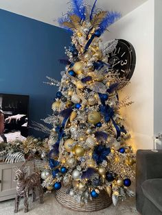 a blue and gold christmas tree in a living room with a clock on the wall