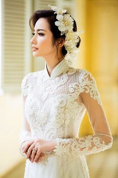 a woman wearing a white dress with flowers in her hair and holding her hand on her hip