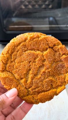 a person holding up a cookie in front of an oven