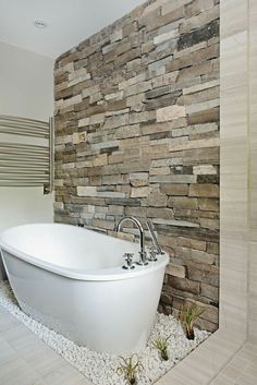 a white bath tub sitting next to a stone wall in a bathroom with pebbles on the floor