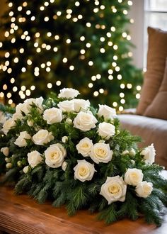 white roses and greenery on a table in front of a christmas tree