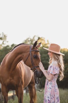 a woman in a dress and hat petting a horse