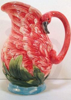 a pink flamingo shaped pitcher sitting on top of a blue base with green leaves