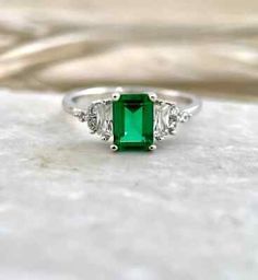 an emerald and diamond ring with three diamonds on the side, set in white gold