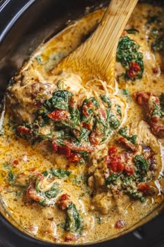 a crock pot filled with chicken and spinach covered in gravy, topped with a wooden spoon