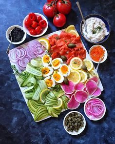 an assortment of vegetables are arranged on a cutting board with dips and sauces