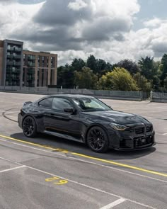 a black sports car parked in an empty parking lot next to some buildings and trees