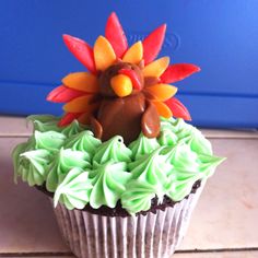 there is a cupcake with icing and a turkey decoration on top, sitting on the table