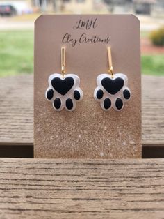 black and white heart shaped paw print earrings on a wooden table next to a card