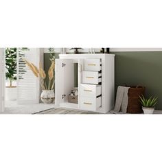 a white cabinet with three drawers in front of a green wall and potted plant