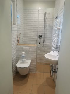 a white toilet sitting next to a sink in a bathroom near a shower head mounted on a wall