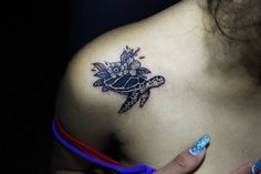 a woman's shoulder with a turtle and flowers tattoo on her left side breast