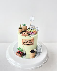 a birthday cake decorated with potted plants and gardening tools on a white platter